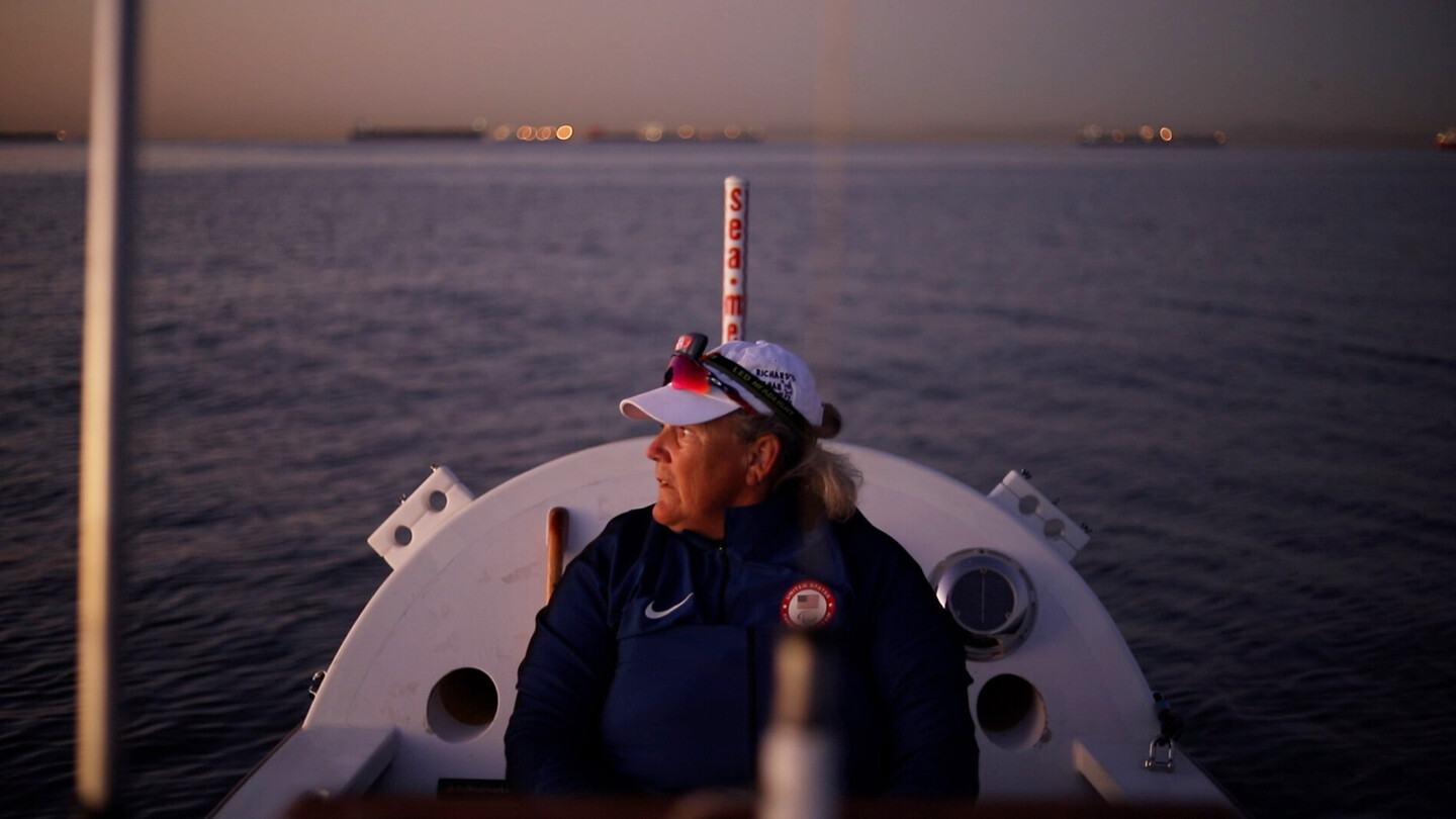 Femme en tenue de sport assise sur un bateau à rames au crépuscule, regardant l’eau calme.
