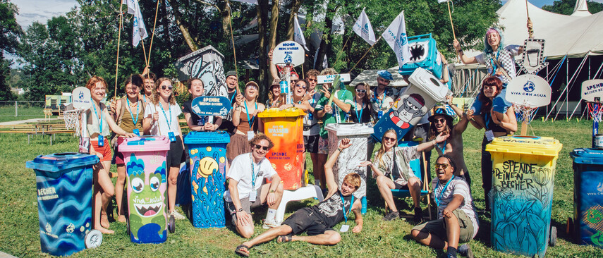 Eine Gruppe mit bunten bemalten M&uuml;lltonnen und Viva Con Agua Schildern und Flaggen